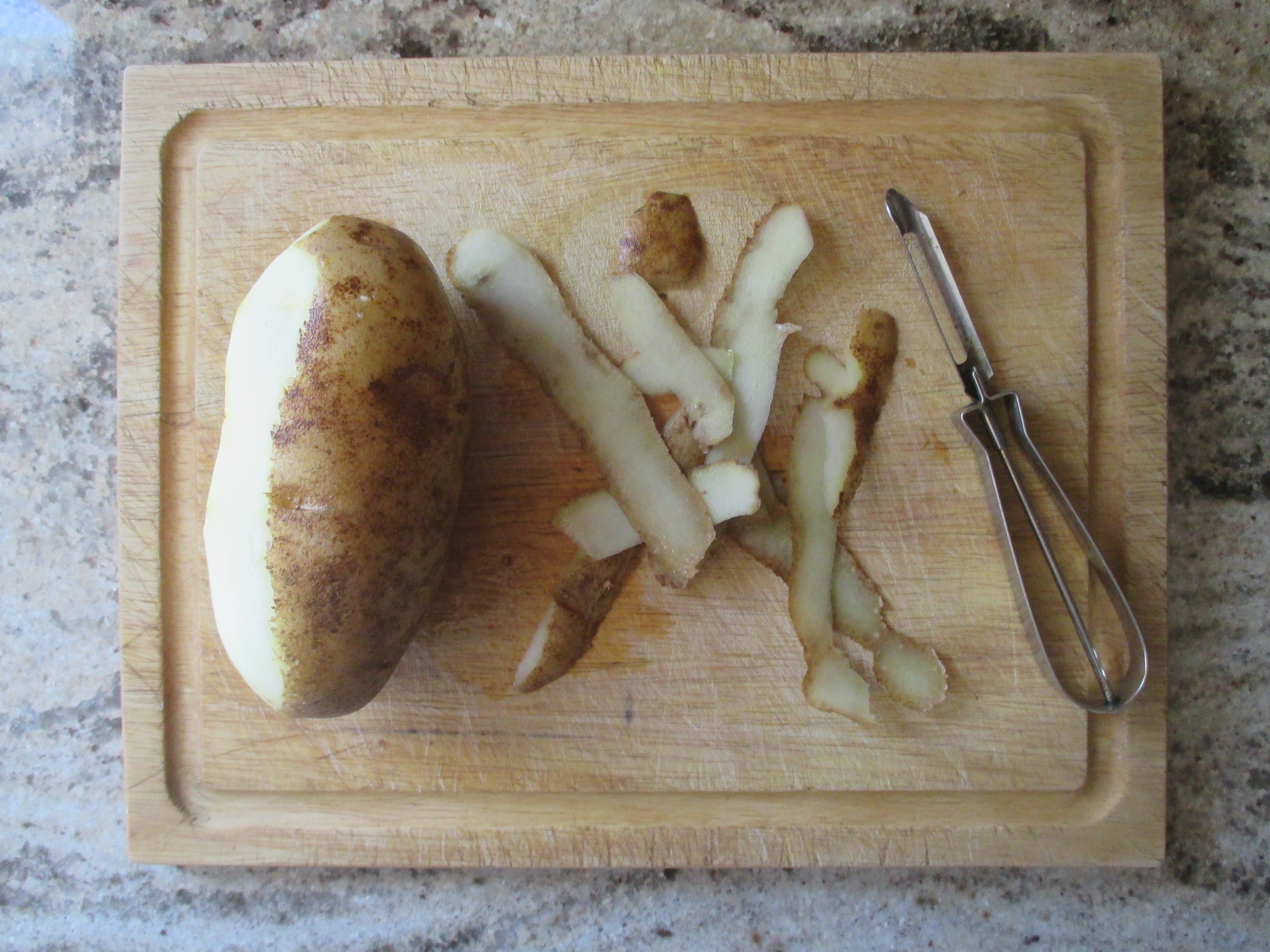 potato, potato peels, and peeler on a cutting board
