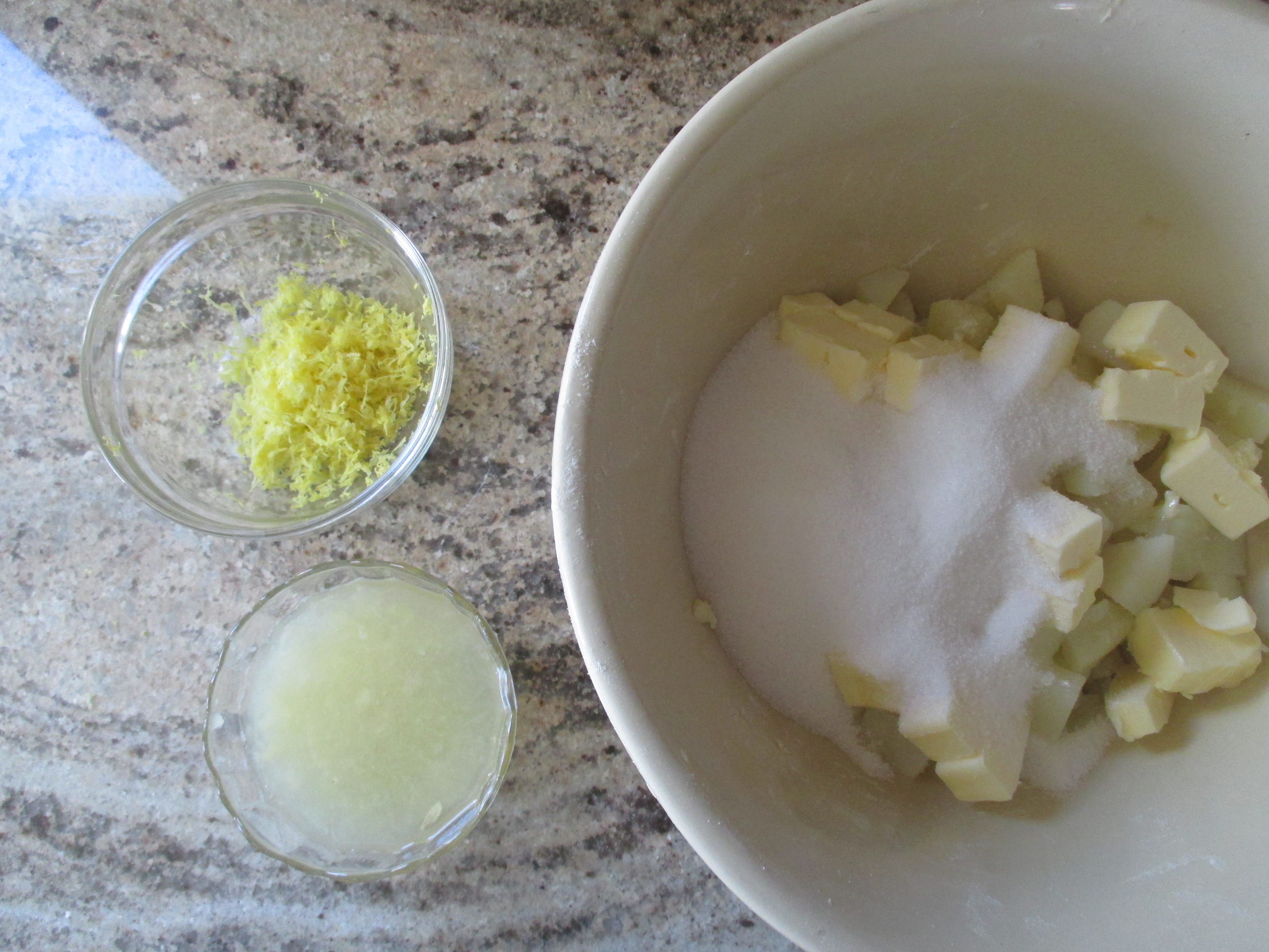 three bowls: one filled with lemon juice, one filled with lemon zest, one with sugar, butter, and cooked potato pieces