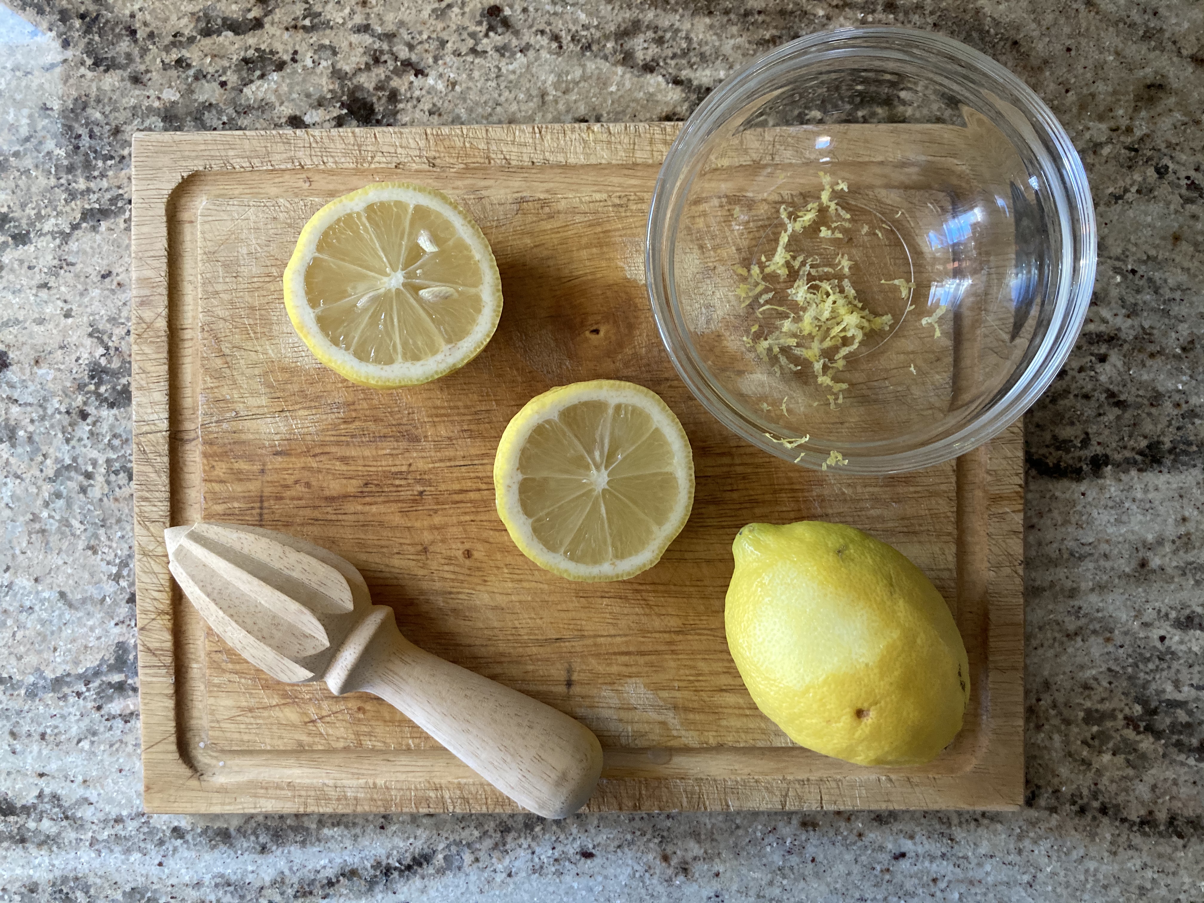 halved lemon, whole lemon, lemon zest, and lemon reamer on a cutting board