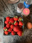 strawberries in pint container on counter next to egg, spice jars, rosewater bottle