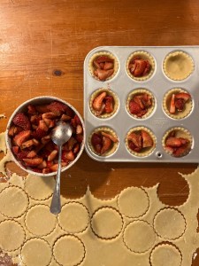 seasoned strawberries filling pastry tart shells, lids in foreground