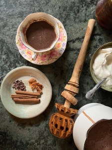 counter with hot chocolate in cup, plate with spices, hot chocolate whisk, cooking tools