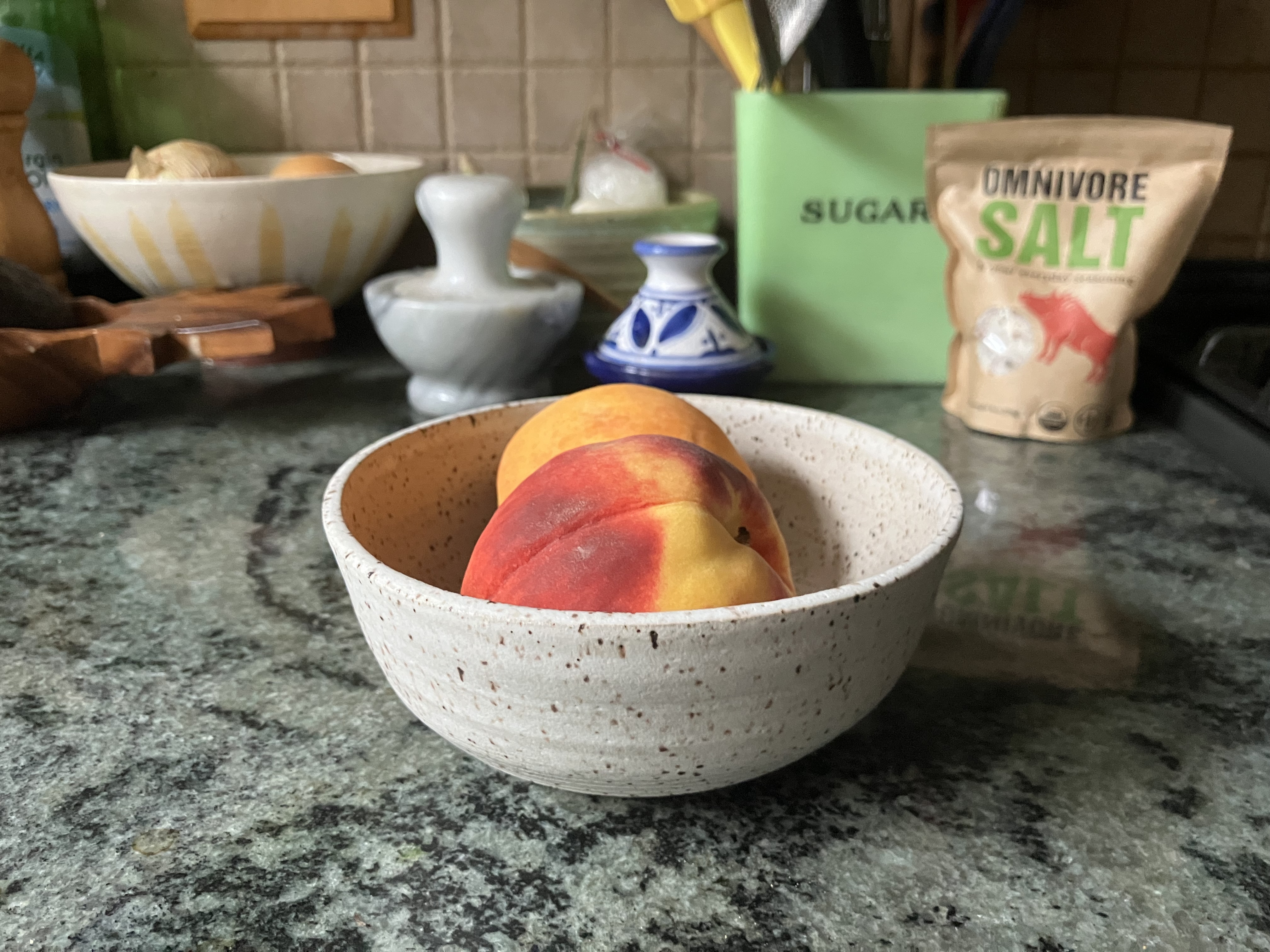 two peaches in a white bowl on a kitchen counter