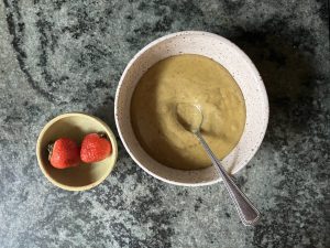 pistachio cream in bowl with spoon with two strawberries in smaller bowl